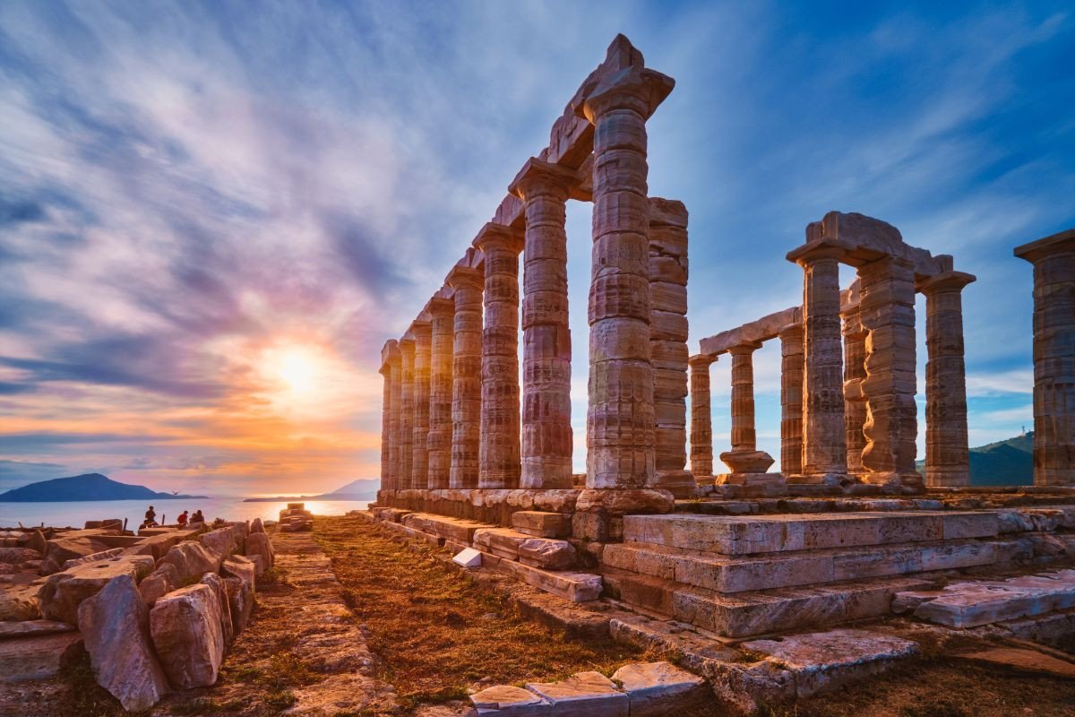 Ancient temple ruins with tall columns at Cape Sounio, set against a vibrant sunset over the sea.
